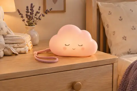 Veilleuse rechargeable rose en forme de nuage posée sur une table de chevet en bois clair
