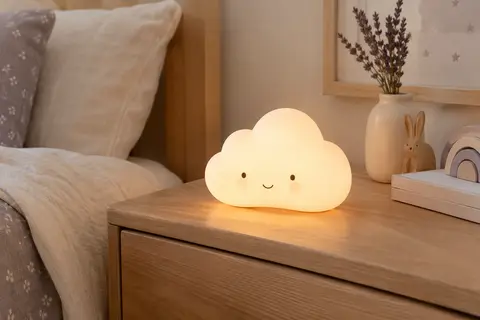 Veilleuse nuage blanche en silicone posée sur une table de chevet en bois clair dans une chambre de bébé
