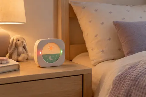 Réveil éducatif FiveHome avec veilleuse, posé sur une table de chevet en bois dans une chambre de bébé.