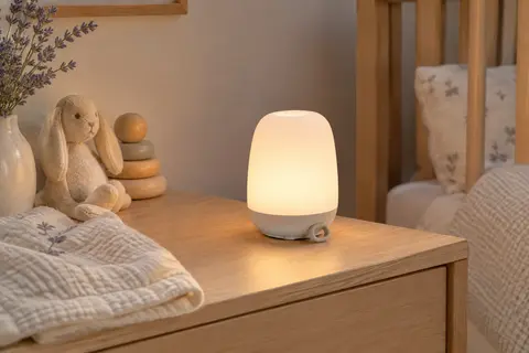Veilleuse rechargeable blanche à lumière chaude posée sur une table de chevet en bois clair.