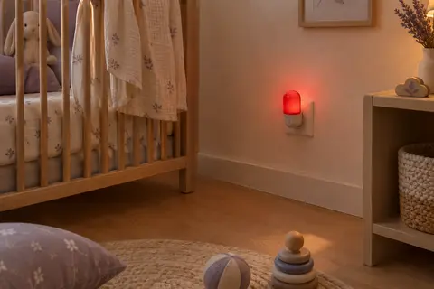 Veilleuse rouge compacte branchée au mur dans une chambre de bébé claire au décor apaisant