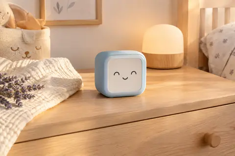Réveil éducatif Mella bleu arctique posé sur une commode en bois clair dans une chambre de bébé.
