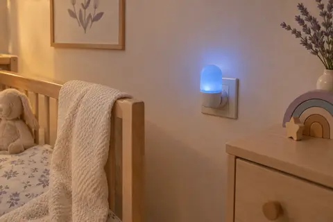 Petite veilleuse bleue branchée dans une chambre de bébé, diffusant une lumière douce près du mur.